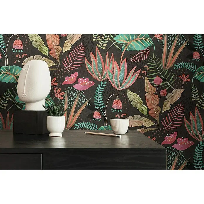 A.S. Création Famous Garden Vliestapete - Schwarz-Bunt-Grün, Floral, 10,05 x 0,53 m - Produktaufnahme mit einer weißen Skulptur, einer Pflanze im Topf und einer Tasse auf einem schwarzen Tisch vor einer bunten floralen Tapete.