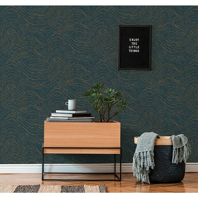 A.S. Création Jade 2 Vliestapete - Dunkelblau-Gold, 3D-Optik, 10,05 x 0,53 m - Elegantes Interieur mit einer Kommode, darauf eine Pflanze, Bücher und eine Tasse, vor einer Wand mit stilvollem Wellenmuster.