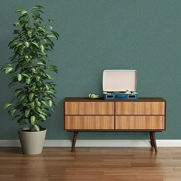 A.S. Création Famous Garden Vliestapete - Petrolblau, Uni, 10,05 x 0,53 m - Elegantes Sideboard aus Holz mit Schallplattenspieler und Kopfhörern, ergänzt durch eine stilvolle Zimmerpflanze vor einer dezenten Wand.