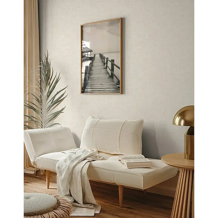 A.S. Création Jade 2 Vliestapete - Creme-Beige, Uni, 10,05 x 0,53 m - Ein gemütlicher Raum mit einem stilvollen, beigen Lounge-Sessel, einem dekorativen Gemälde und einer goldenen Lampe.