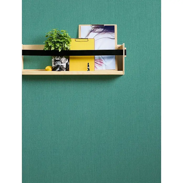 A.S. Création Stories of Life Vliestapete - Smaragdgrün, Uni, 10,05 x 0,53 m - Ein Wandregal aus Holz mit Pflanzen, einem gelben Notizblock und einem Bild an einer grünen Wand. Das Regal ist mit einem schwarzen Band versehen.