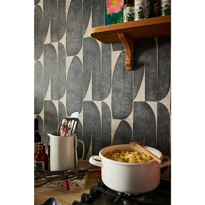 A.S. Création Stories of Life Vliestapete - Beige-Schwarz, Floral, 10,05 x 0,53 m - Ein Küchenstillleben mit einem weißen Topf voller Spaghetti auf dem Herd vor einer gemusterten Tapete und einem rustikalen Holzregal.