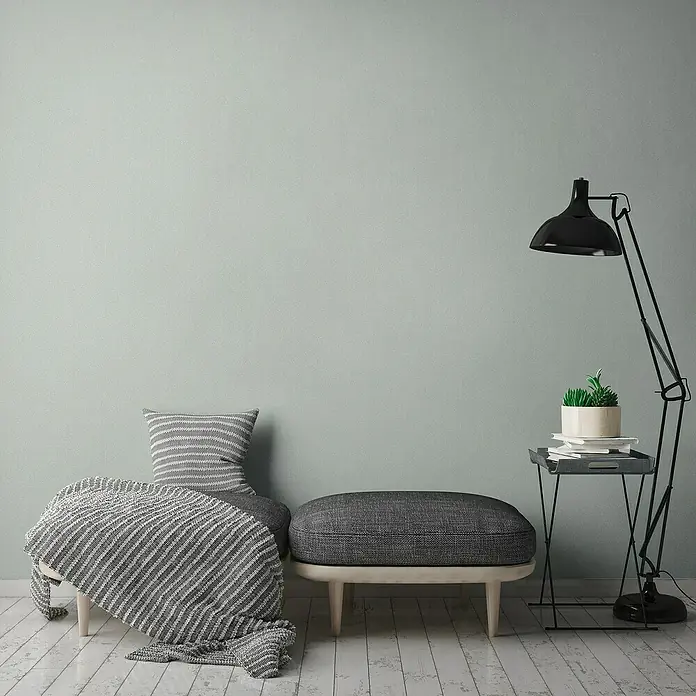 A.S. Création Jade 2 Vliestapete - Mintgrün, Uni, 10,05 x 0,53 m - Einladende Ecke mit gepolsterter Bank, Kissen und Decke in Grauweiß, akzentuiert durch eine Stehlampe und einen Beistelltisch mit Pflanze.