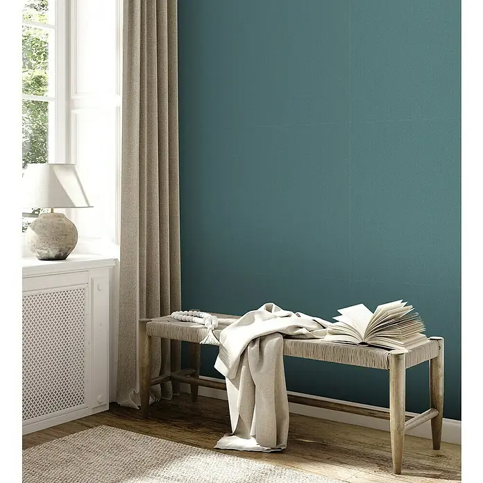 A.S. Création Jade 2 Vliestapete - Grün-Blau, Uni, 10,05 x 0,53 m - Dekorative Szene mit einer rustikalen Holzbank, auf der ein Buch und ein Tuch liegen, neben einem Fenster mit Vorhang und einer Lampe.
