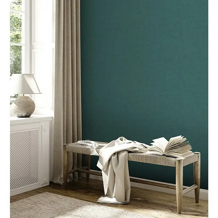 A.S. Création Jade 2 Vliestapete - Petrol, Uni, 10,05 x 0,53 m - Ein gemütlicher Raum mit einer Bank, einem Buch und einer Decke vor einer grünen Wand.