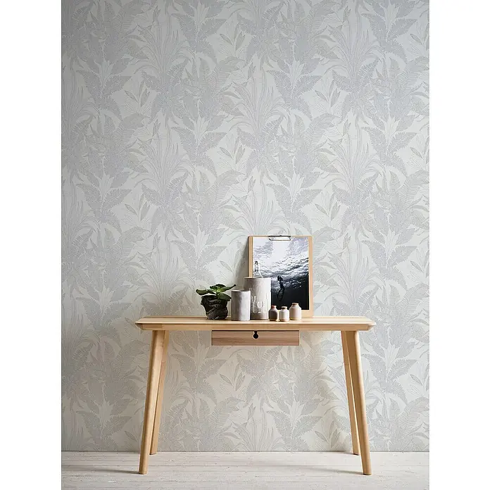 A.S. Création Stories of Life Vliestapete Dschungel - Grau-Creme-Gold, Floral, 10,05 x 0,53 m - Ein stilvoller Konsolentisch aus hellem Holz mit einer Schublade und diversen Dekorationsartikeln, vor einer dezenten Blättertapete.