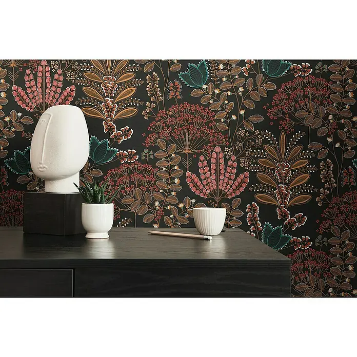 A.S. Création Famous Garden Vliestapete - Schwarz-Bunt-Petrol, Floral, 10,05 x 0,53 m - Nahaufnahme einer Tischdekoration mit Keramikgesicht, Pflanze, Schale und Bleistift vor floral gemusterter Wand.