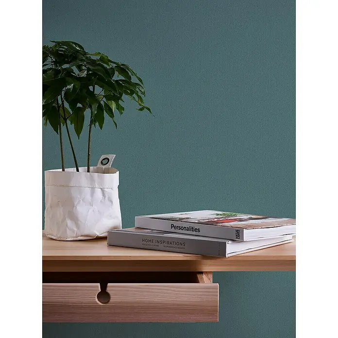 A.S. Création Jade 2 Vliestapete - Grün-Blau, Uni, 10,05 x 0,53 m - Das Bild zeigt einen Schreibtisch mit einer Zimmerpflanze und zwei Büchern, die eine ruhige und stilvolle Arbeitsumgebung schaffen.
