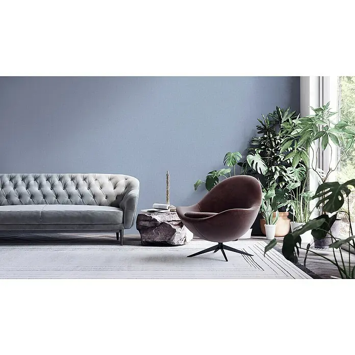 A.S. Création Famous Garden Vliestapete - Blau, Uni, 10,05 x 0,53 m - Das Bild zeigt ein stilvolles Wohnzimmer mit einem grauen Sofa und einem braunen Sessel, ergänzt durch Grünpflanzen.