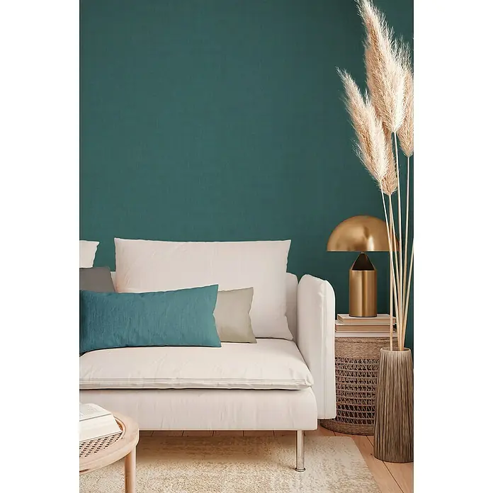A.S. Création Jade 2 Vliestapete - Petrol, Uni, 10,05 x 0,53 m - Elegantes Wohnzimmer mit weißem Sofa, Zierkissen und einer goldenen Lampe, die eine warme und einladende Atmosphäre schaffen.