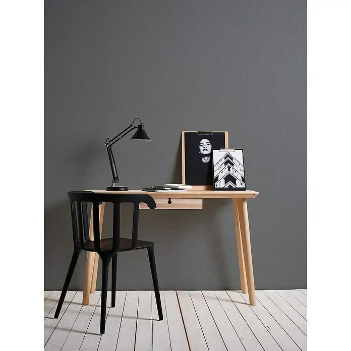 A.S. Création Stories of Life Vliestapete - Anthrazit-Grau, Uni, 10,05 x 0,53 m - Moderner Arbeitsplatz mit hellem Schreibtisch, schwarzem Stuhl und Lampe, dekoriert mit Bilderrahmen.