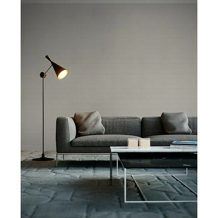 A.S. Création Jade 2 Vliestapete - Weiß/Gold, Grafisch, 10,05 x 0,53 m - Elegantes Wohnzimmer mit grauem Sofa, modernem Couchtisch und einer stilvollen Stehlampe, die warmes Licht spendet.