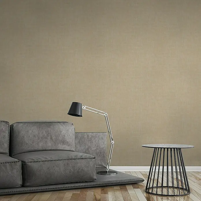 A.S. Création Jade 2 Vliestapete - Beige-Taupe, Uni, 10,05 x 0,53 m - Nahaufnahme eines grauen Sofas, einer Lampe und eines Tisches vor einem neutralen Hintergrund.