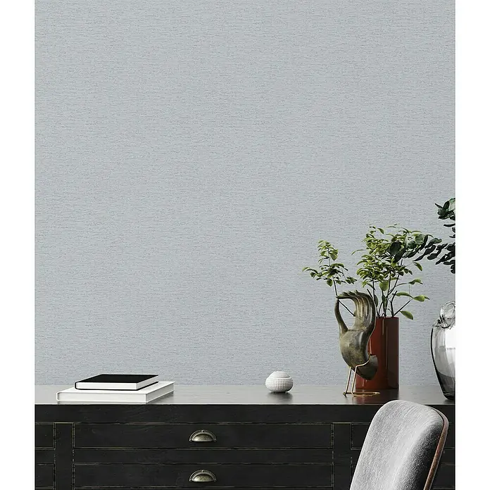 A.S. Création Famous Garden Vliestapete - Grau-Hellgrau, Uni, 10,05 x 0,53 m - Nahaufnahme eines stilvollen Tisches mit Dekorationen, Büchern und Pflanzen vor einer grauen Wand.