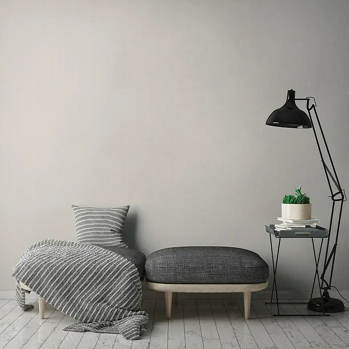 A.S. Création Jade 2 Vliestapete - Creme-Weiß, Uni, 10,05 x 0,53 m - Gemütliche Leseecke mit grauem Sitzmöbel, Kissen und Decke, ergänzt durch eine Stehlampe und einen kleinen Tisch.