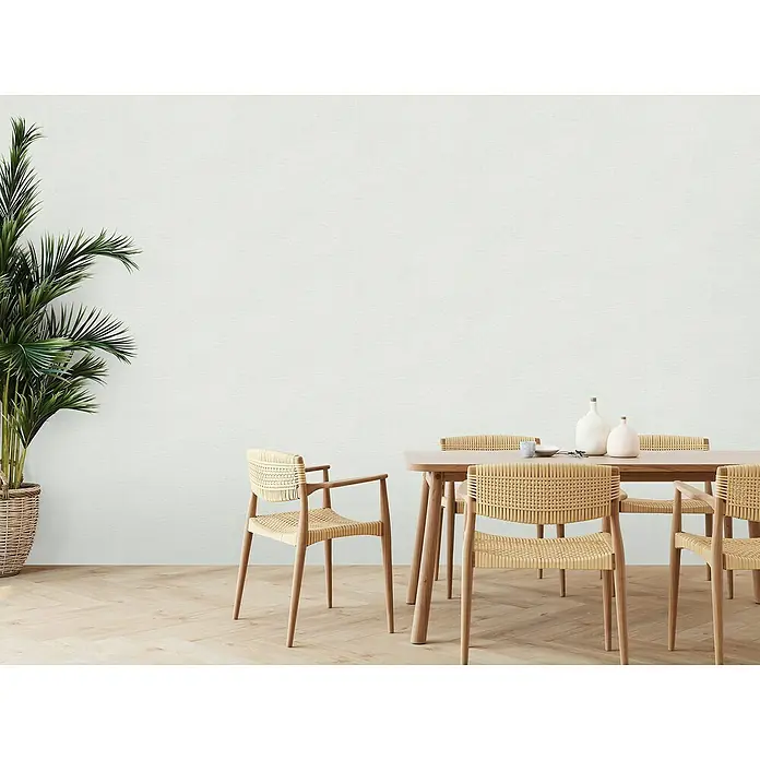 A.S. Création Famous Garden Vliestapete - Grau-Weiß, Uni, 10,05 x 0,53 m - Ein heller Essbereich mit einem Holztisch und Stühlen aus Rattan. Die Zimmerpflanze und die minimalistische Deko sorgen für eine ruhige Atmosphäre.
