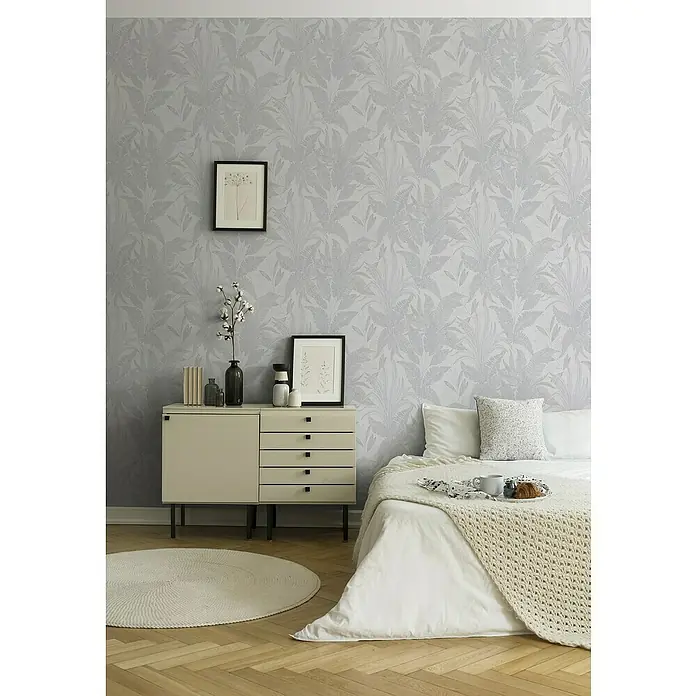 A.S. Création Stories of Life Vliestapete Dschungel - Grau-Creme-Gold, Floral, 10,05 x 0,53 m - Ein Schlafzimmer mit einem dekorierten Nachttisch, einem Bett mit Decke und einem runden Teppich auf einem Holzboden.