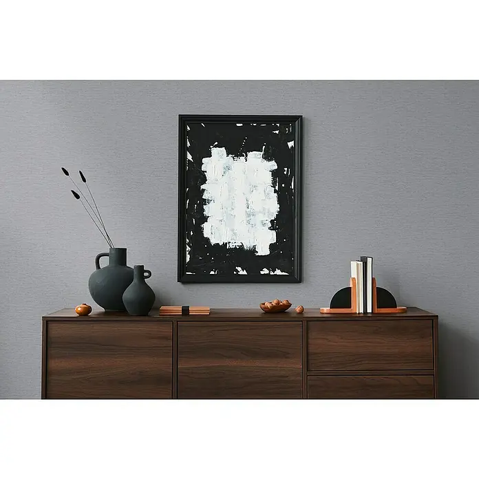 A.S. Création Famous Garden Vliestapete - Mittelgrau, Uni, 10,05 x 0,53 m - Das Bild zeigt eine moderne Kommode aus Holz mit einem abstrakten Gemälde, Vasen und dekorativen Buchstützen, die ein stilvolles Ambiente schaffen.