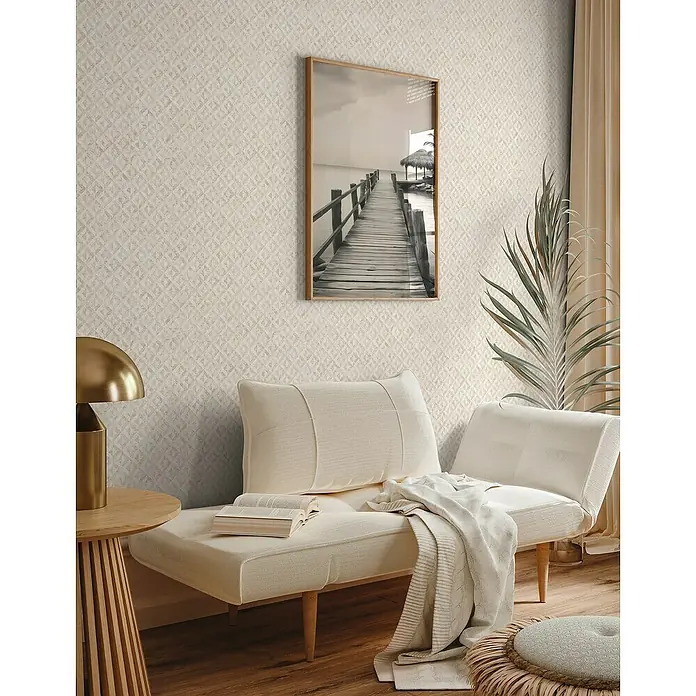 A.S. Création Jade 2 Vliestapete - Weiß-Gold, Grafisch, 10,05 x 0,53 m - Elegantes Wohnzimmer mit beigem Sofa, Holztisch und gerahmtem Bild an einer gemusterten Wand, die eine gemütliche und stilvolle Atmosphäre schafft.