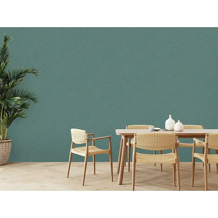 A.S. Création Famous Garden Vliestapete - Petrolblau, Uni, 10,05 x 0,53 m - Ein Esszimmer mit hellen Korbstühlen um einen Esstisch und einer großen Pflanze, die eine gemütliche Atmosphäre schafft.