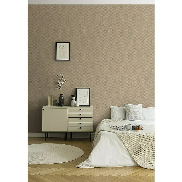A.S. Création Jade 2 Vliestapete - Beige-Gold, Grafisch, 10,05 x 0,53 m - Nahaufnahme eines Schlafzimmers mit beigem Wandmuster, einem weißen Nachttisch und einem Bett mit weißer Bettwäsche.