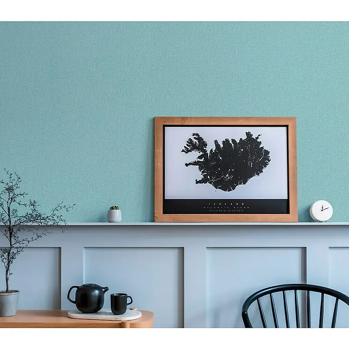 A.S. Création Famous Garden Vliestapete - Türkisblau-Hellblau, Uni, 10,05 x 0,53 m - Ein gerahmtes Island-Poster mit einer Teekanne, einer Tasse und einer Uhr auf einem Regal vor einer blaugrünen Wand.