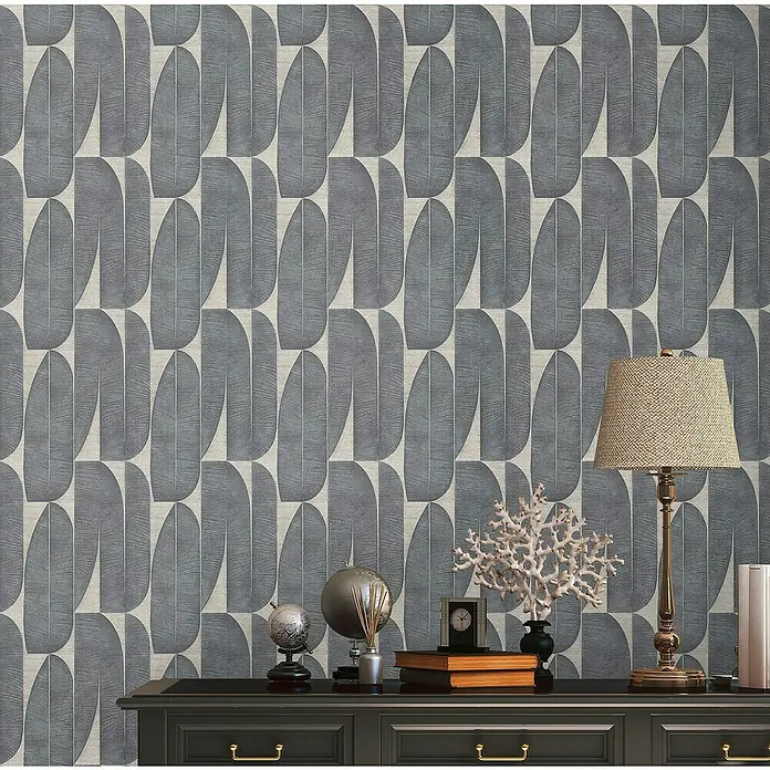 A.S. Création Stories of Life Vliestapete - Beige-Schwarz, Floral, 10,05 x 0,53 m - Eine Nahaufnahme einer Wand mit grauer, abstrakter Blättertapete, die über einem schwarzen Tisch mit dekorativen Gegenständen hängt.