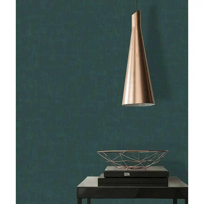 A.S. Création Jade 2 Vliestapete - Dunkles Petrol, Uni, 10,05 x 0,53 m - Dekorative goldene Pendelleuchte mit geometrischer Schale, die auf Büchern auf einem schwarzen Tisch platziert ist, vor einem dunkelgrünen Hintergrund.