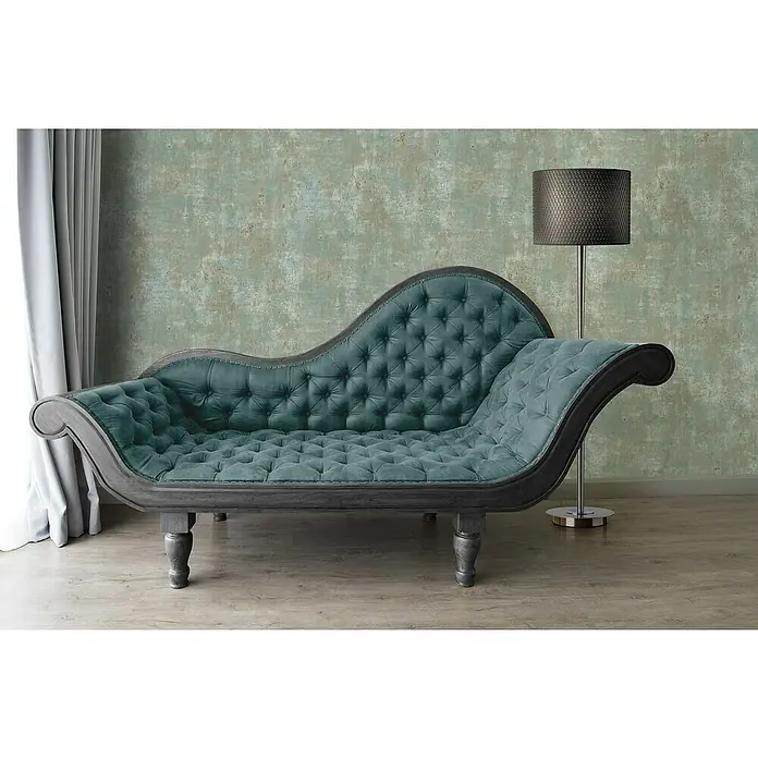 A.S. Création Stories of Life Vliestapete Patina - Salbeigrün-Blau-Gold, Betonoptik, 10,05 x 0,53 m - Elegante türkisfarbene Chaiselongue mit Knopfheftung und dunklem Holzrahmen, perfekt für stilvolle Entspannung. Eine Stehlampe steht daneben.