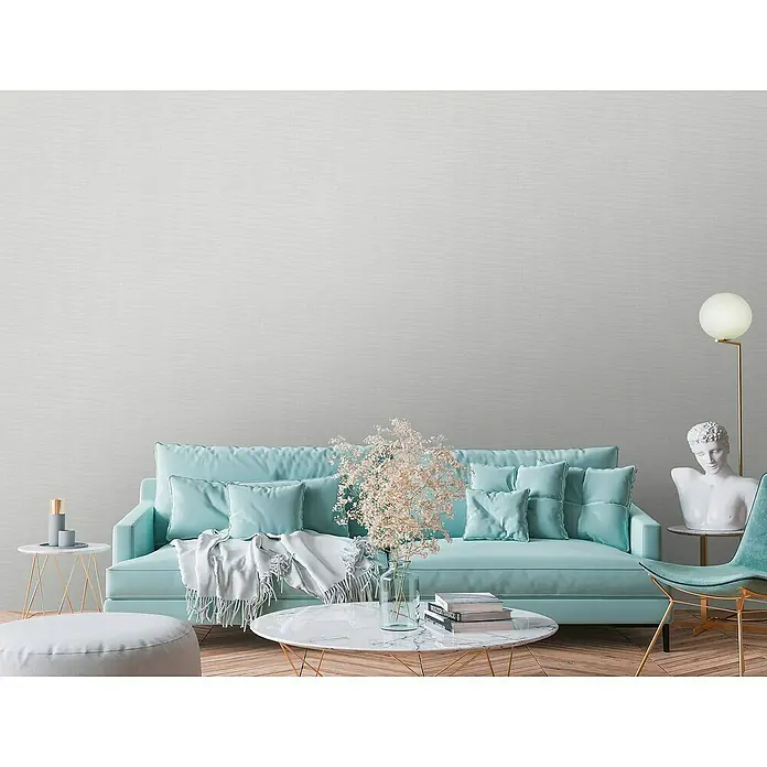 A.S. Création Stories of Life Vliestapete - Betongrau-Hellgrau, Uni, 10,05 x 0,53 m - Elegantes Wohnzimmer mit hellblauer Couch, Marmortisch und dekorativen Elementen, die eine ruhige und stilvolle Atmosphäre schaffen.