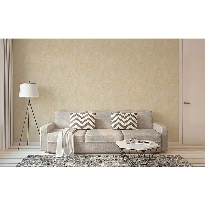 A.S. Création Jade 2 Vliestapete Blätter - Weiß-Beige-Gold, Floral, 10,05 x 0,53 m - Ein gemütliches Wohnzimmer mit einem grauen Sofa, dekorativen Kissen und einem stilvollen Couchtisch, beleuchtet durch eine Stehlampe.