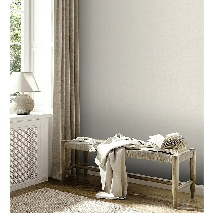 A.S. Création Jade 2 Vliestapete - Creme-Beige, Uni, 10,05 x 0,53 m - Ein gemütliches Interieur mit einer Bank, einem Buch und einer Lampe, das eine entspannende Atmosphäre schafft.