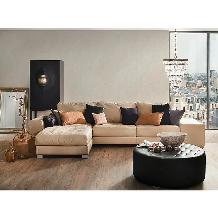 A.S. Création Jade 2 Vliestapete - Cremegrau, Uni, 10,05 x 0,53 m - Beige Ledercouch mit Zierkissen und einem schwarzen Hocker, dekoriert mit Vasen und einer Schale, für eine elegante Wohnzimmeratmosphäre.