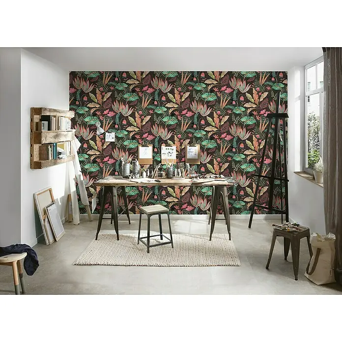 A.S. Création Famous Garden Vliestapete - Schwarz-Bunt-Grün, Floral, 10,05 x 0,53 m - Das Foto zeigt einen Raum mit einer bunten floralen Tapete und einem Holztisch, der als Arbeitsbereich mit Staffelei und diversem Zubehör dient.