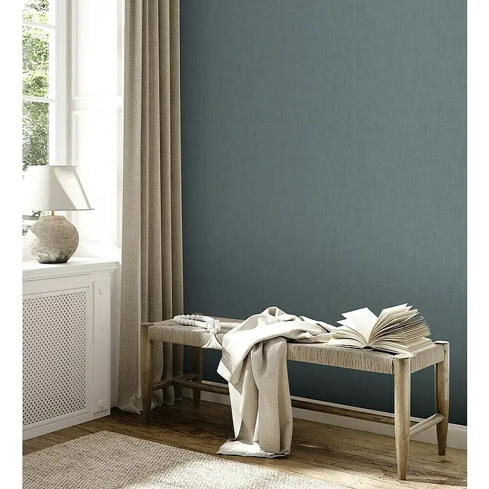 A.S. Création Jade 2 Vliestapete - Blau-Grün, Uni, 10,05 x 0,53 m - Dieses Bild zeigt eine moderne Inneneinrichtung mit einer Bank mit einer Decke und einem aufgeschlagenen Buch darauf, neben einem Fenster.