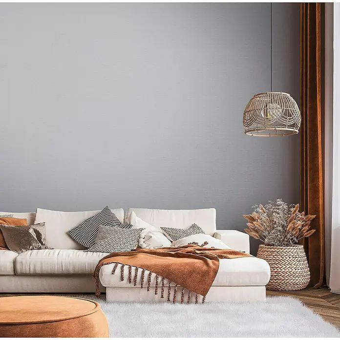 A.S. Création Famous Garden Vliestapete - Mittelgrau, Uni, 10,05 x 0,53 m - Elegantes Wohnzimmer-Interieur mit beigem Sofa, Zierkissen, Überwurf und dekorativer Hängelampe für eine gemütliche Atmosphäre.