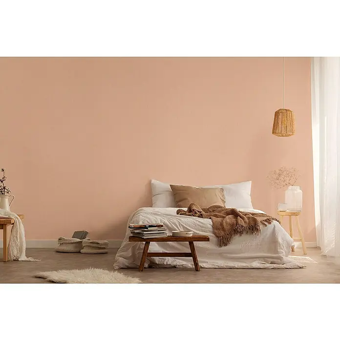 A.S. Création Jade 2 Vliestapete - Rosa-Orange, Uni, 10,05 x 0,53 m - Schlafzimmer mit einem Bett mit weißer Bettwäsche, einer Strickdecke und einem Holzschemel mit Büchern davor.
