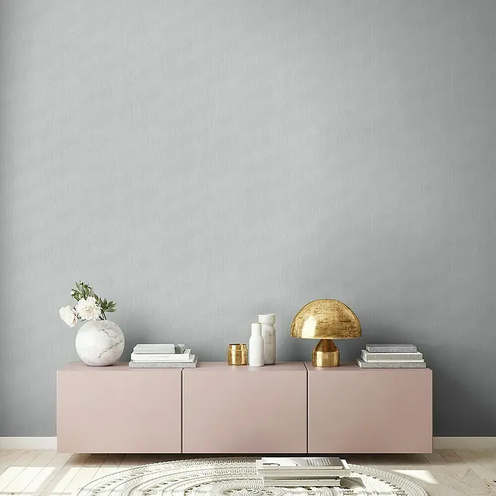 A.S. Création Stories of Life Vliestapete - Grau, Uni, 10,05 x 0,53 m - Einrichtungsidee mit einem rosa Sideboard, einer goldenen Lampe und dekorativen Elementen wie Vasen und Büchern vor einer grauen Wand.