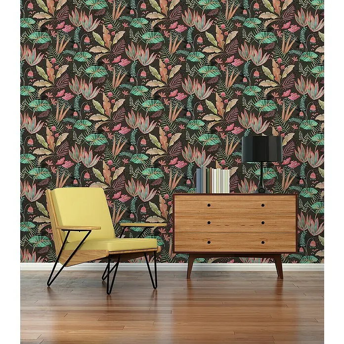 A.S. Création Famous Garden Vliestapete - Schwarz-Bunt-Grün, Floral, 10,05 x 0,53 m - Einrichtung mit einem hellgelben Sessel und einer Holzkommode vor einer bunten Blumentapete.