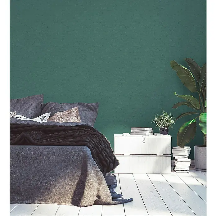 A.S. Création Famous Garden Vliestapete - Petrol-Grün, Uni, 10,05 x 0,53 m - Schlafzimmerinterieur mit einem stilvollen Bett mit grauer Bettwäsche und einem Beistelltisch mit Pflanzen und Büchern.