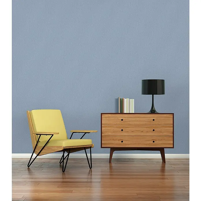 A.S. Création Famous Garden Vliestapete - Blau, Uni, 10,05 x 0,53 m - Gelber Sessel neben Holzkommode mit Lampe und Büchern vor blauer Wand. Elegantes Möbeldesign für stilvolle Innenräume.
