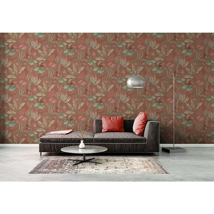 A.S. Création Famous Garden Vliestapete - Rot-Orange-Grün, Floral, 10,05 x 0,53 m - Wohnzimmer mit Terrakotta-Blättertapete, grauer Couch, Teppich und Stehlampe. Gemütliches Interieur mit stilvollem Muster und moderner Einrichtung.