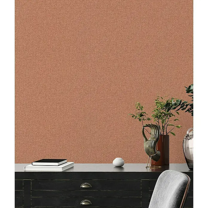 A.S. Création Famous Garden Vliestapete - Rot-Orange, Uni, 10,05 x 0,53 m - Nahaufnahme einer schwarzen Kommode mit Deko-Elementen wie Bücher, Vase und einer Skulptur vor einer gemusterten Wand.