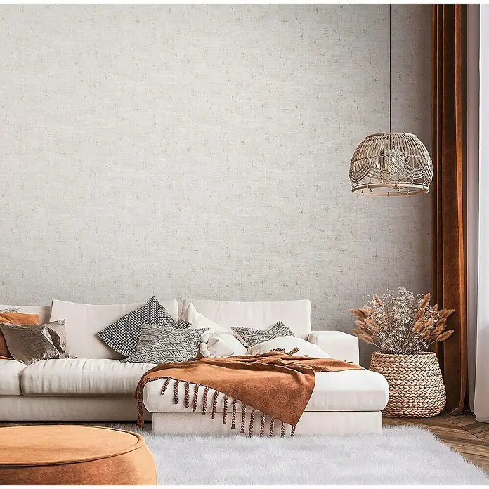 A.S. Création Stories of Life Vliestapete - Grau-Cremeweiß-Gold, Uni, 10,05 x 0,53 m - Elegantes Wohnzimmer mit einem weißen Sofa, dekorativen Kissen und einer stilvollen braunen Tagesdecke, das ein gemütliches Ambiente schafft.