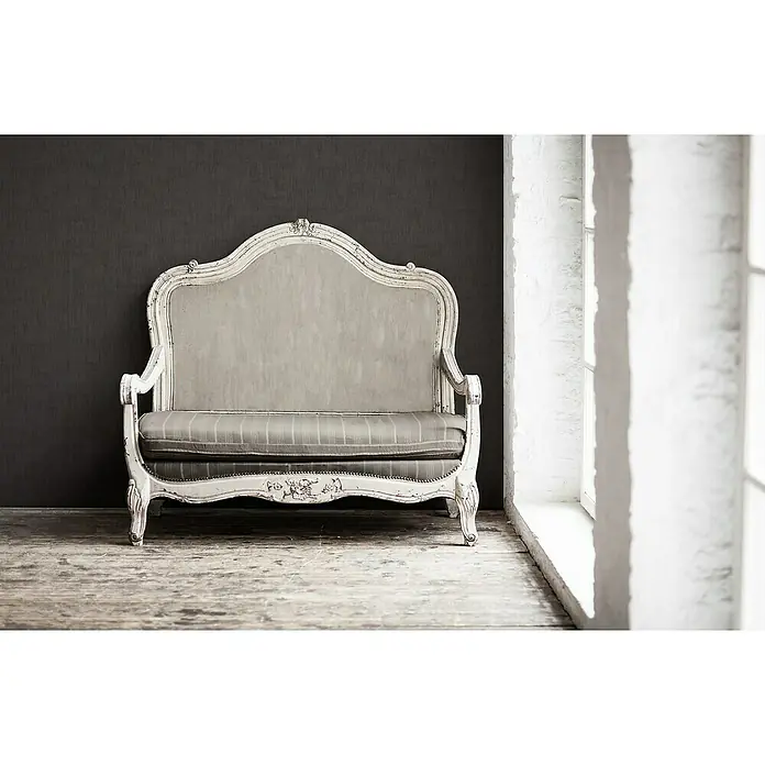 A.S. Création Jade 2 Vliestapete - Schwarz, Uni, 10,05 x 0,53 m - Antikes Sofa mit weiß gestrichenem Rahmen und gestreiftem Sitzkissen vor dunkler Wand und hellem Fenster.