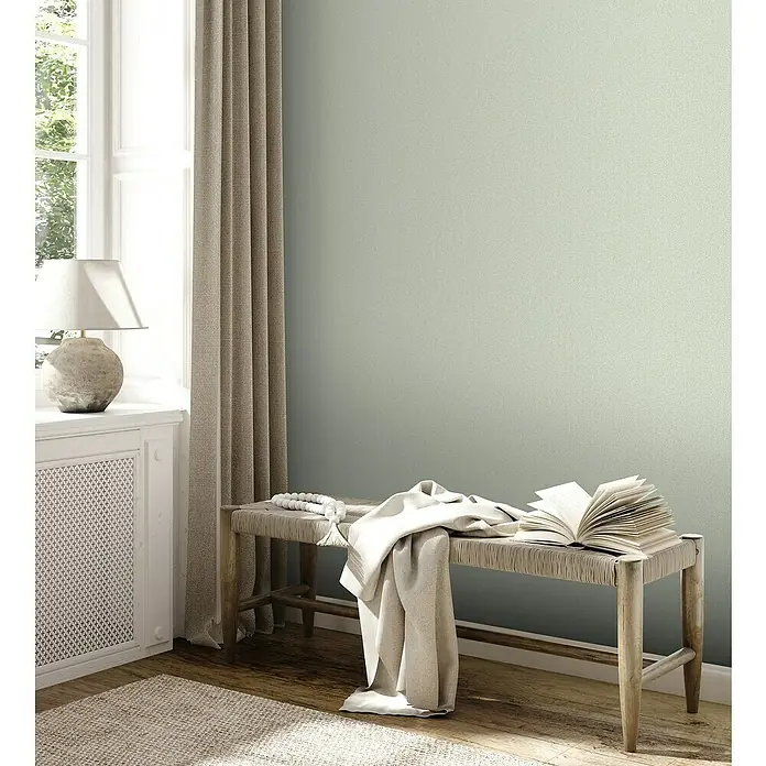 A.S. Création Jade 2 Vliestapete - Pastellgrün, Uni, 10,05 x 0,53 m - Elegante Szene mit einer Bank, einem Buch und einer Lampe, die eine gemütliche und stilvolle Atmosphäre schafft. Die Bank lädt zum Verweilen ein.