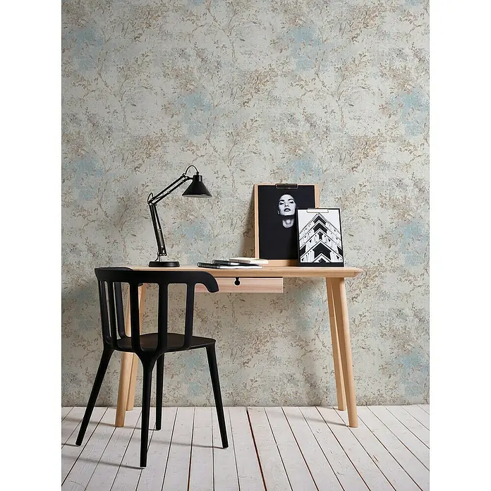 A.S. Création Stories of Life Vliestapete Zweig - Blau-Beige-Gold, Floral, 10,05 x 0,53 m - Stilvoller Arbeitsplatz mit einem hellen Holzschreibtisch, einer schwarzen Lampe und einem schwarzen Stuhl vor einer gemusterten Wand.
