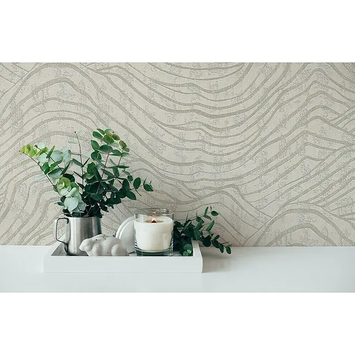 A.S. Création Jade 2 Vliestapete - Weiß-Silber, 3D-Optik, 10,05 x 0,53 m - Stillleben mit einer weißen Kerze, einem Metallkrug mit Eukalyptus und einer Hasenfigur auf einem weißen Tablett vor einer gemusterten Wand.