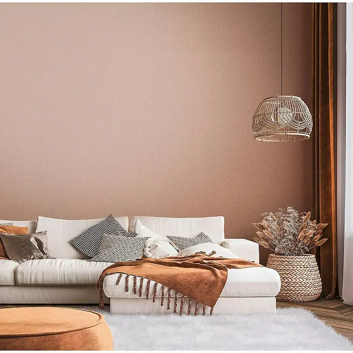 A.S. Création Famous Garden Vliestapete - Rot-Orange, Uni, 10,05 x 0,53 m - Wohnzimmer mit weißem Sofa, Zierkissen und einer braunen Decke auf einer Ottomane, die ein gemütliches Ambiente schafft.