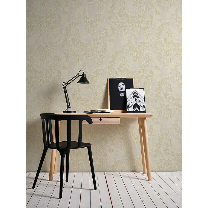 A.S. Création Jade 2 Vliestapete Blätter - Weiß-Beige-Gold, Floral, 10,05 x 0,53 m - Schwarzer Stuhl an einem Holztisch mit Lampe, Notizbuch und Bildern. Das Zimmer hat eine dezent gemusterte Tapete und einen Holzboden.